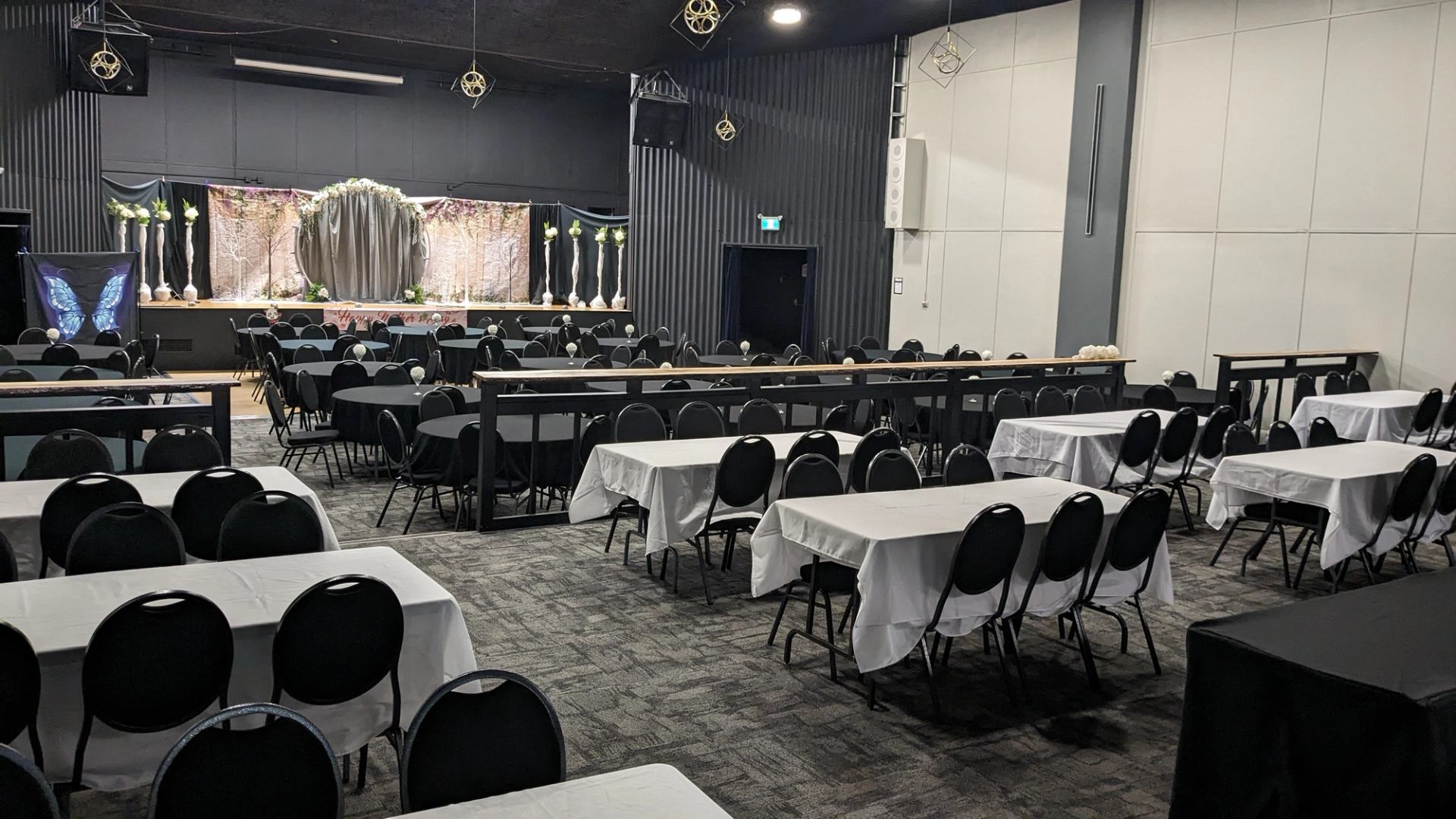 Banquet hall with round and rectangular tables facing a decorated stage with arch.