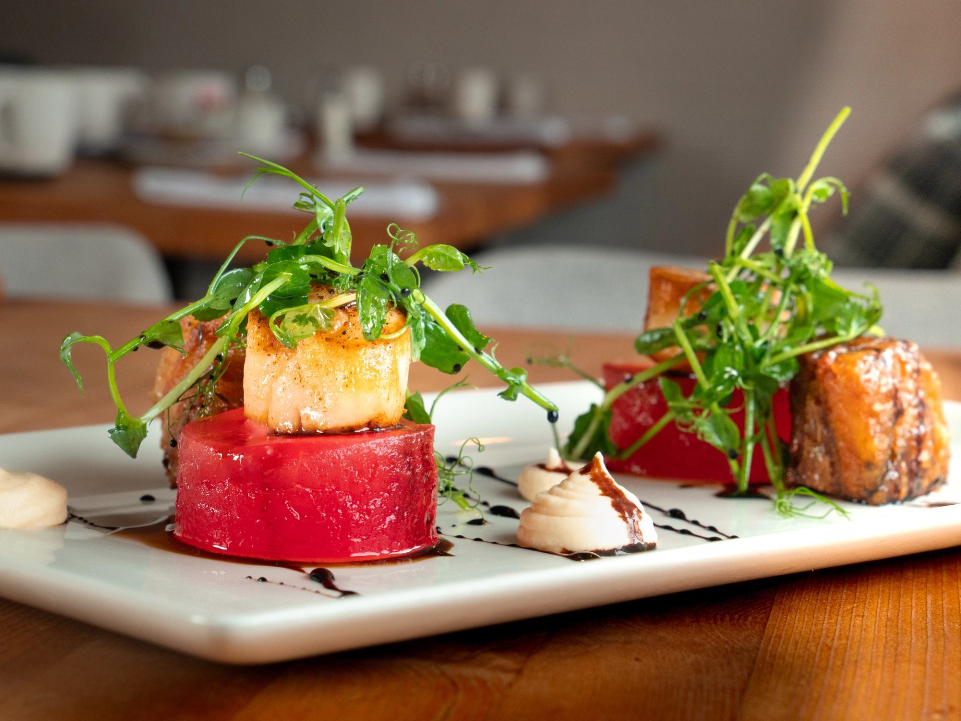 Gourmet plate with scallops, seared meat, greens, and artistic sauce presentation.