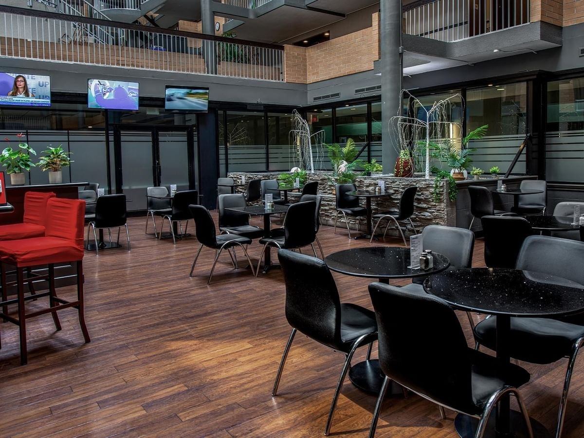 Atrium dining area with black tables, chairs, plants and wall-mounted televisions.