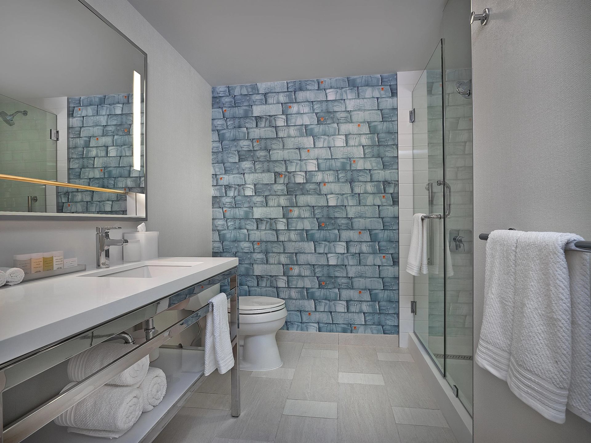 Modern hotel bathroom with blue tile, glass shower, and sleek vanity.