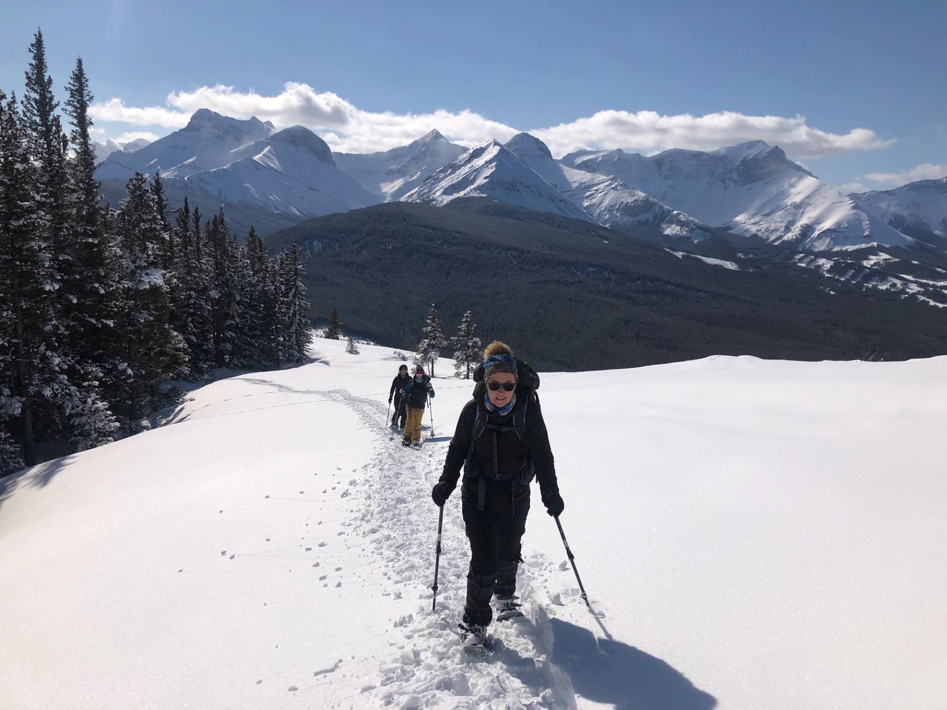 Snowshoers trekking across a snowy ridge with mountain peaks in the background.