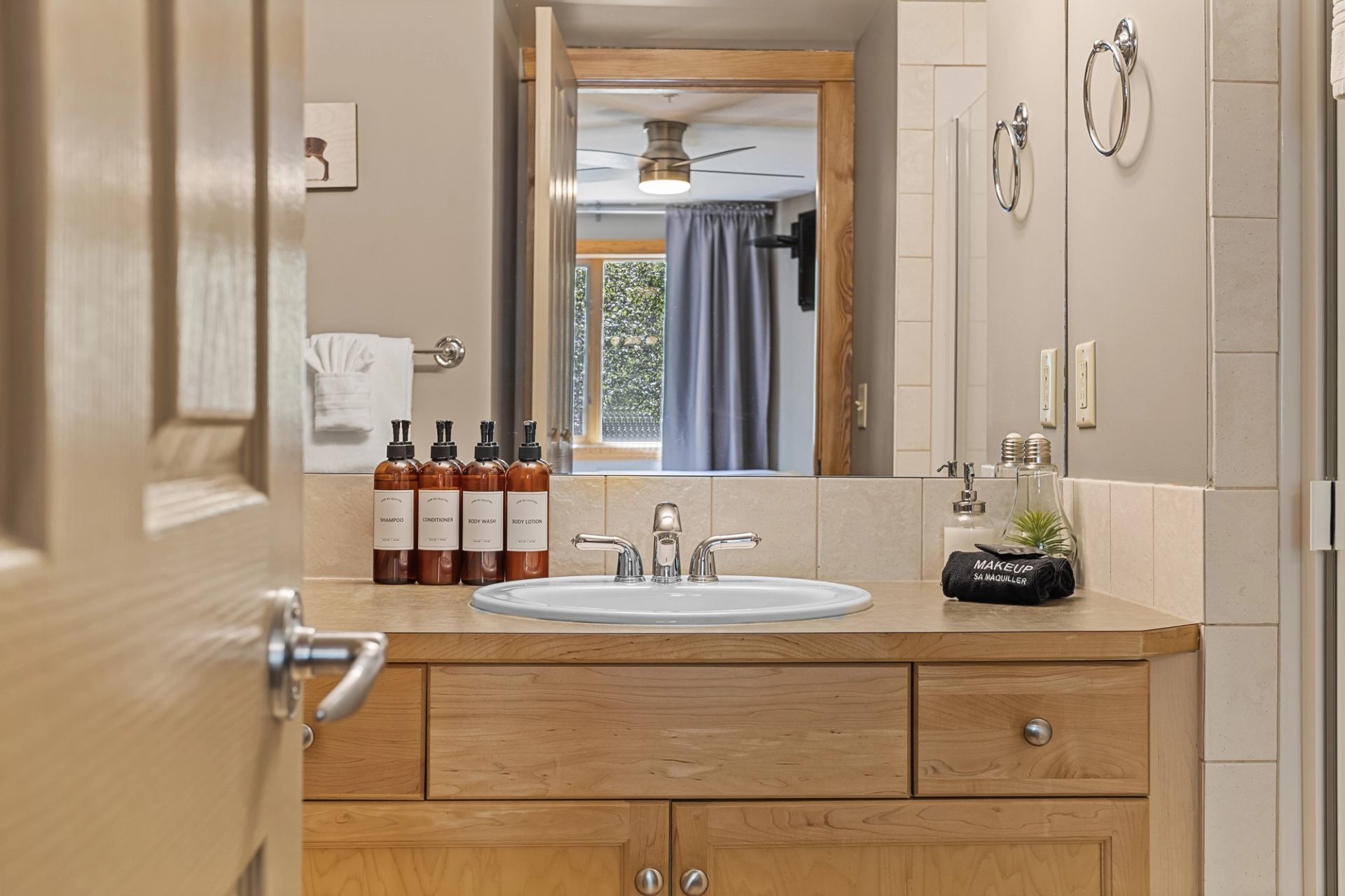 Bathroom with wooden vanity, sink, mirror, and neatly arranged bottles of toiletries.