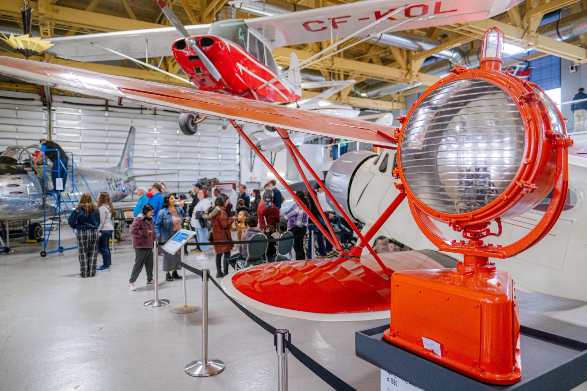Bright red aircraft and spotlight on display with visitors exploring exhibits at The Hangar Flight Museum.