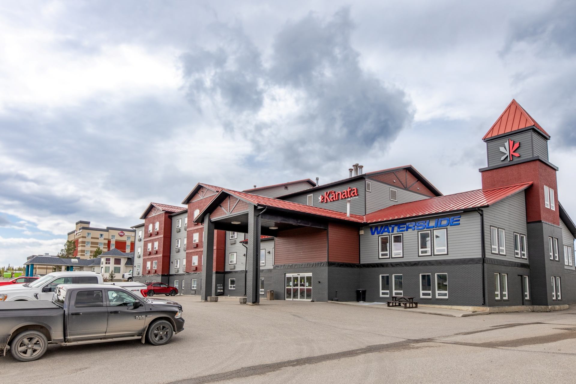 Kanata hotel with red roofs, waterslide signage and parked vehicles under cloudy skies.