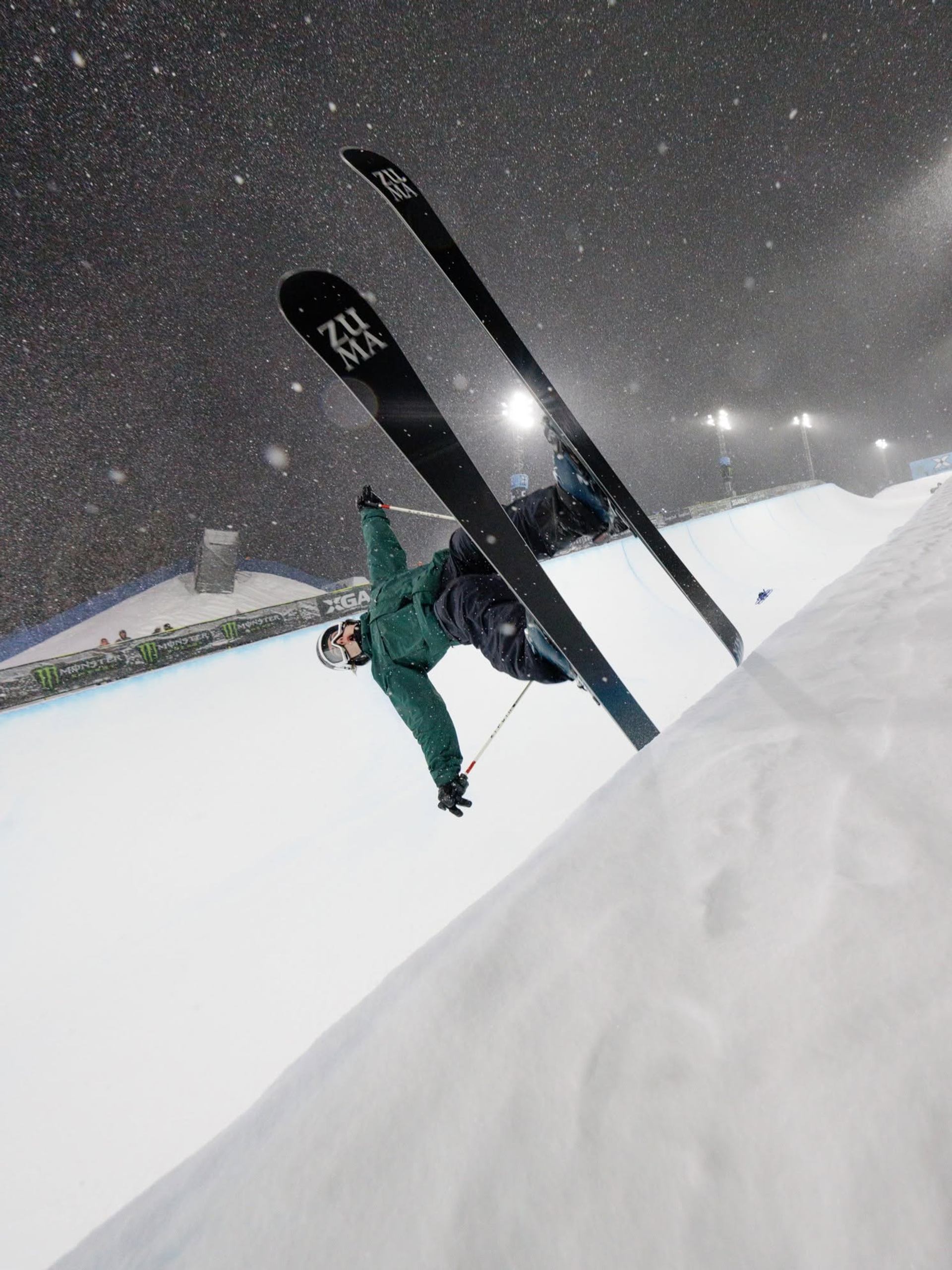 Skier performs an inverted aerial trick above a snow-covered course during heavy snowfall.