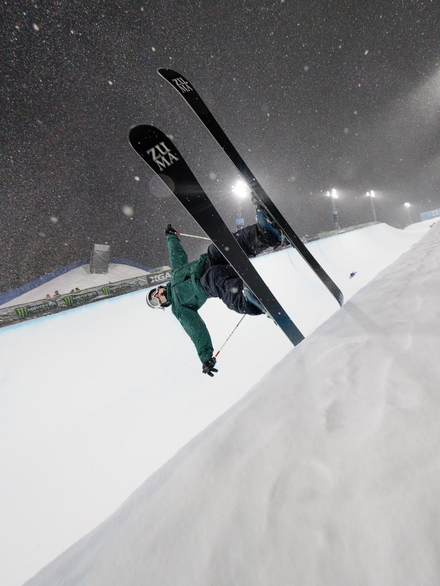 Skier performs an inverted aerial trick above a snow-covered course during heavy snowfall.