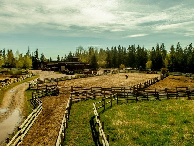 Scenic ranch with wooden fences, open fields, and distant buildings.