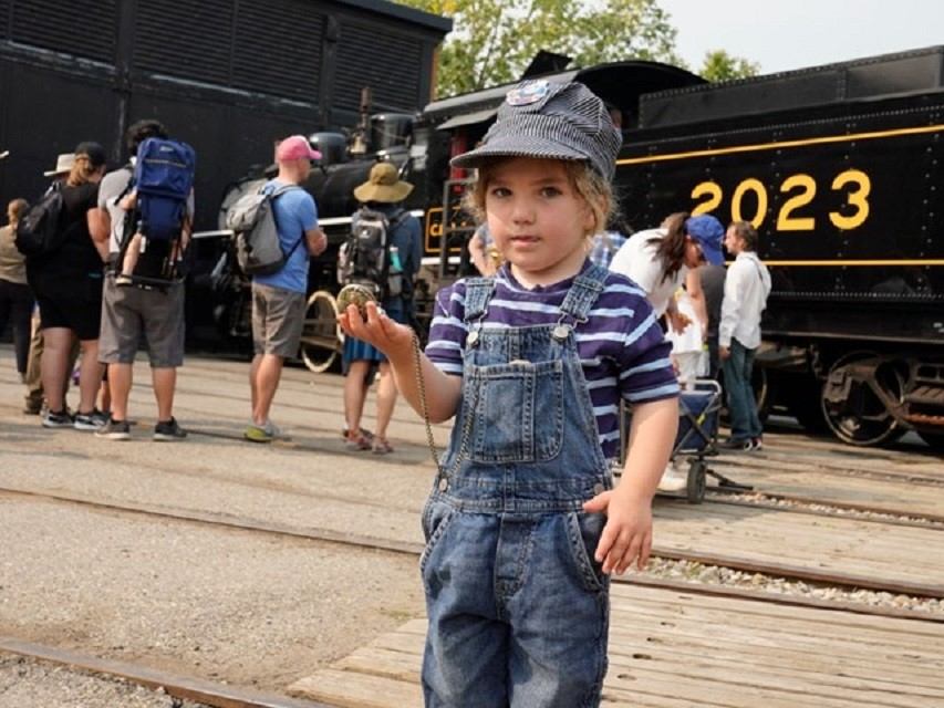 Child in conductor hat near steam train at Heritage Park.