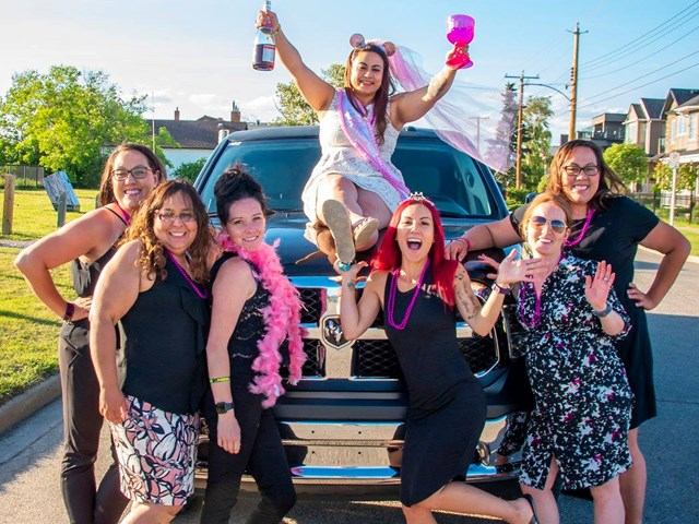 Group celebrating in front of a black party bus with festive outfits and accessories.