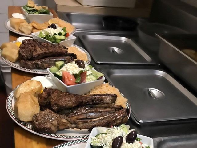 Plates of grilled lamb chops with Greek salad, rice, and bread rolls.