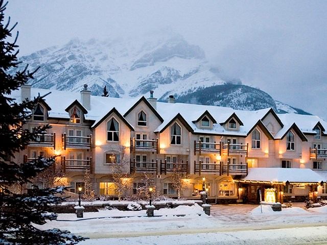 Snowy Rundlestone Lodge with warm lights and mountain backdrop.