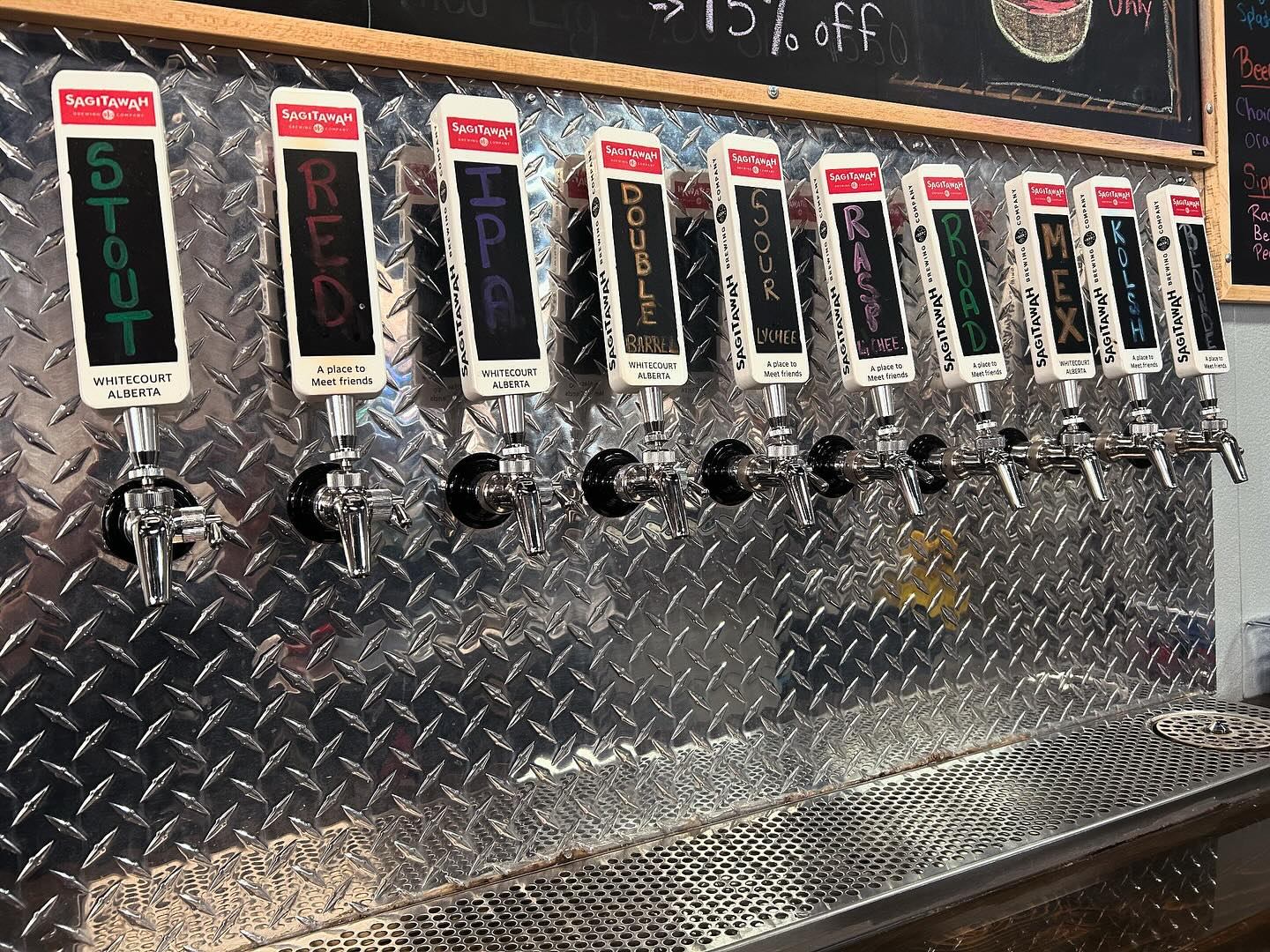 Sagitawah Brewing Company tap handles on diamond-plate bar, with a chalkboard behind them.