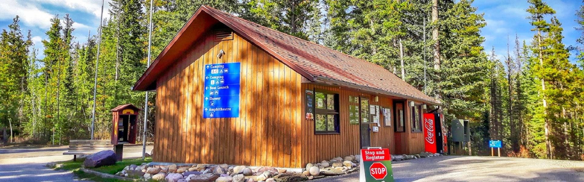 Wooden campground registration building with stop sign, blue directions, and Coca-Cola machine.