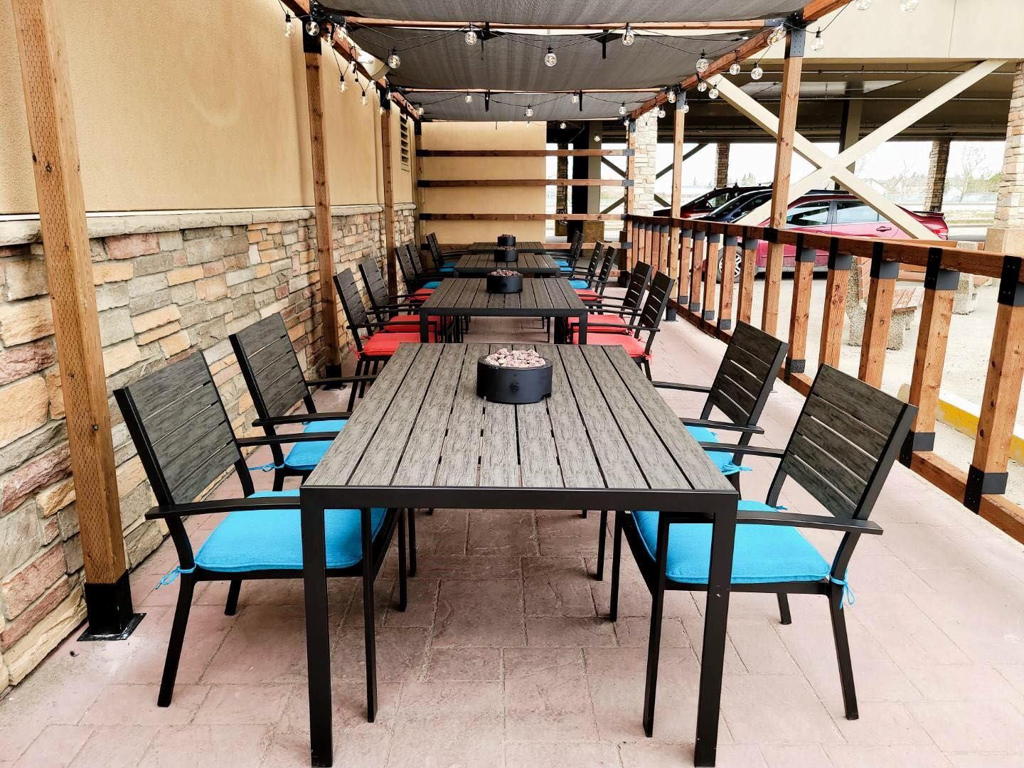 Outdoor dining with fire pits, string lights, and blue-cushioned chairs under pergola.