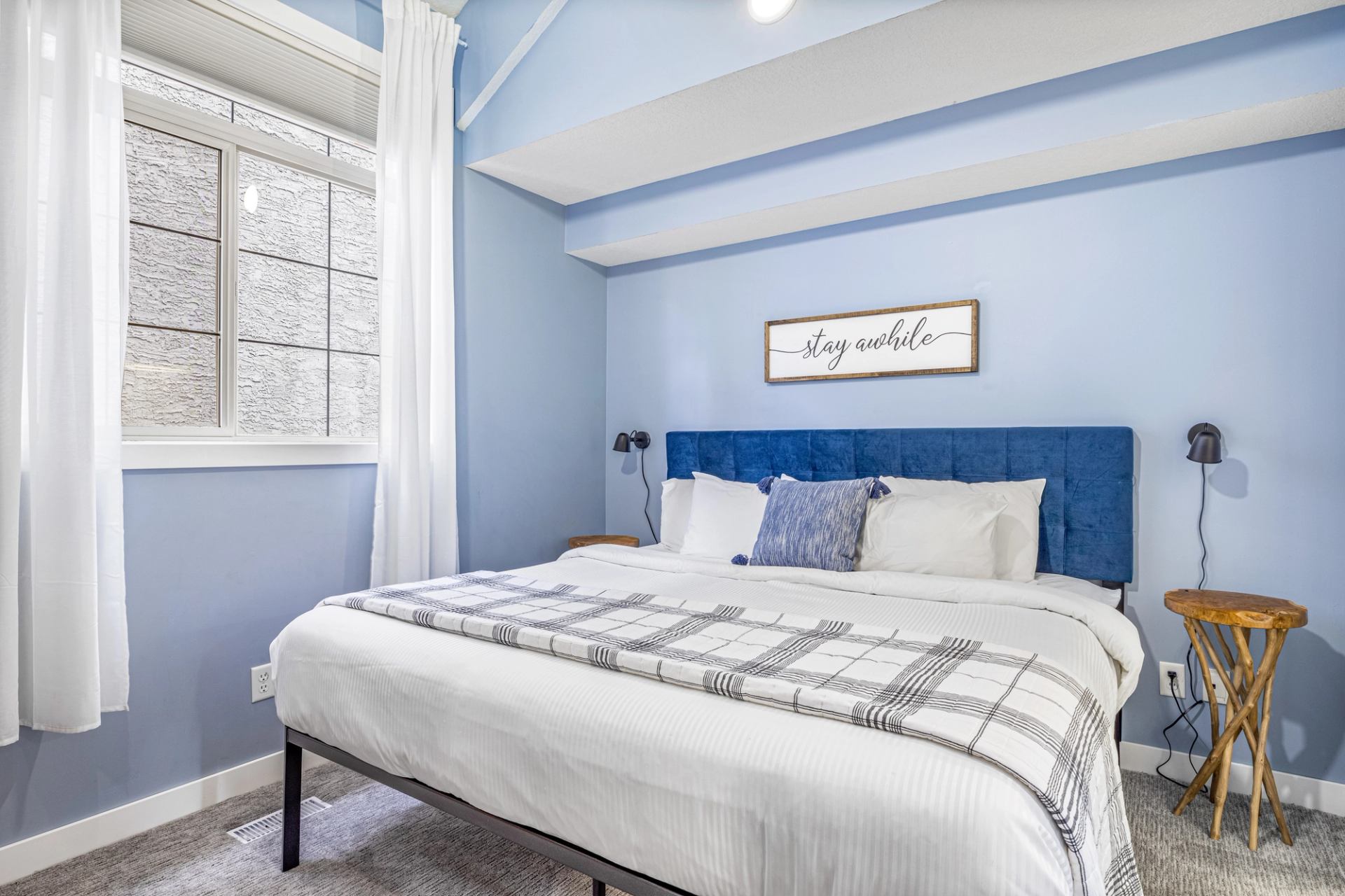 Bedroom with blue walls, white bedding, blue headboard, window and wooden side tables.