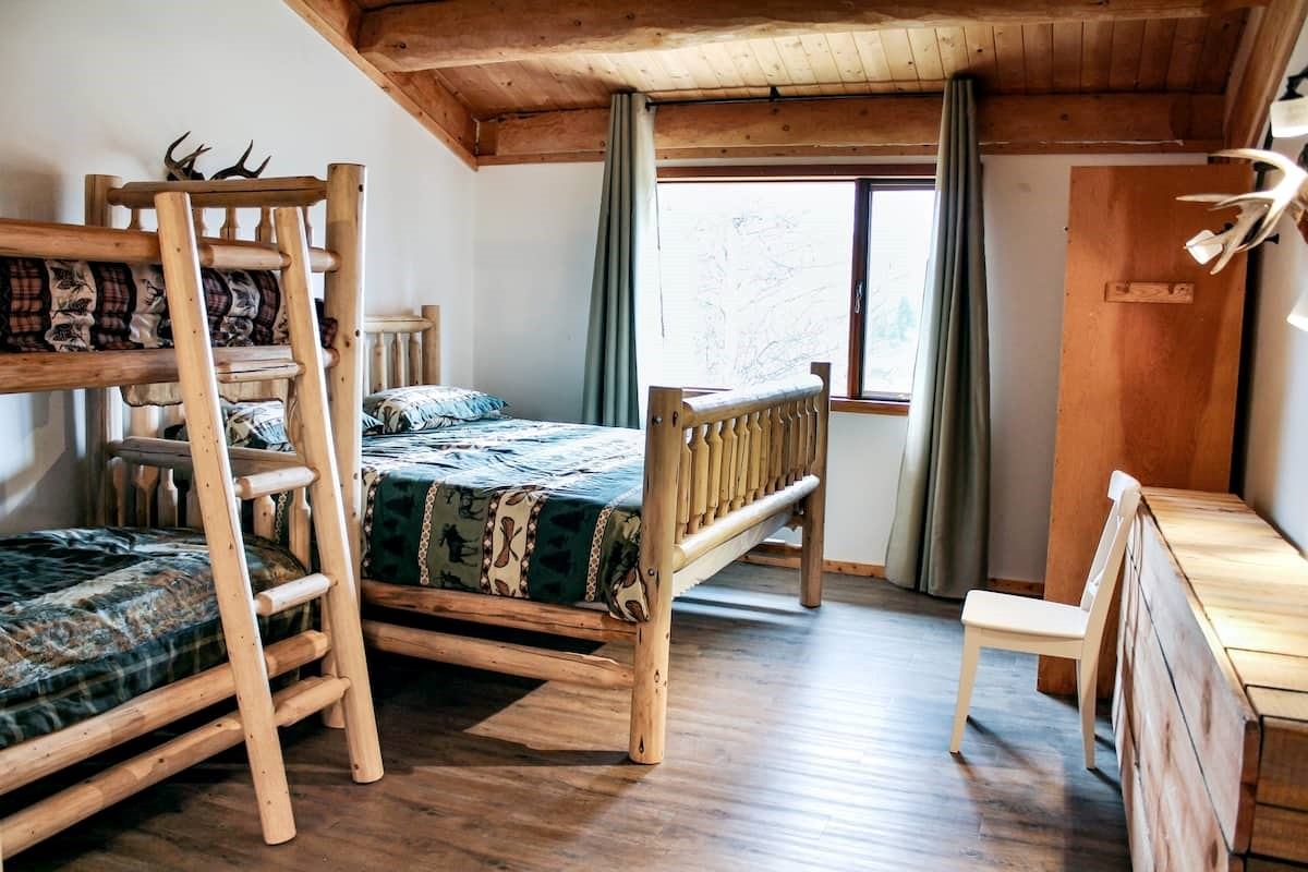 Rustic bedroom with wooden bunk beds and a single bed, featuring nature-themed bedding at Rock Lake Lodge.