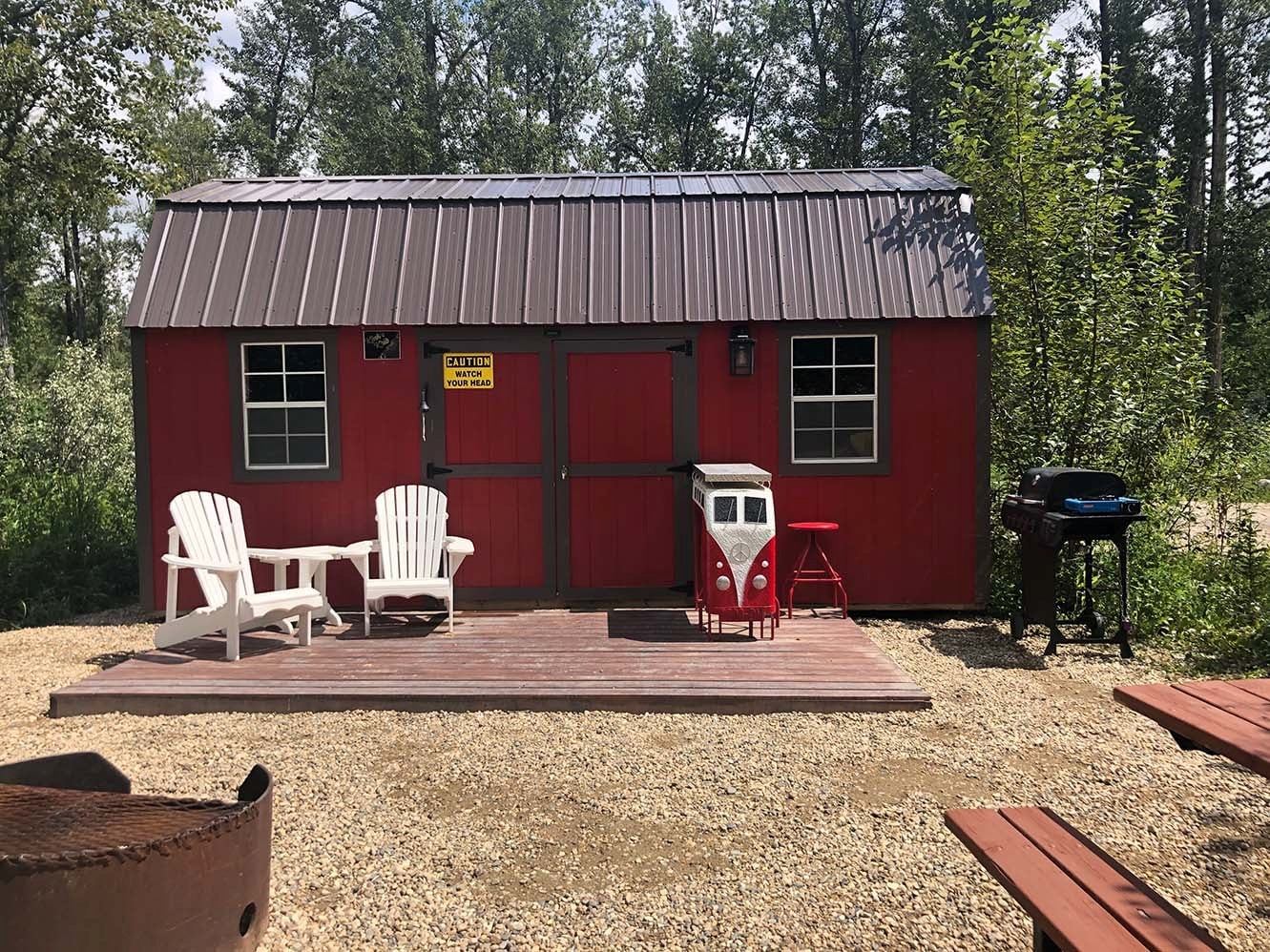 Red cabin with porch seating, BBQ, and fire pit area
