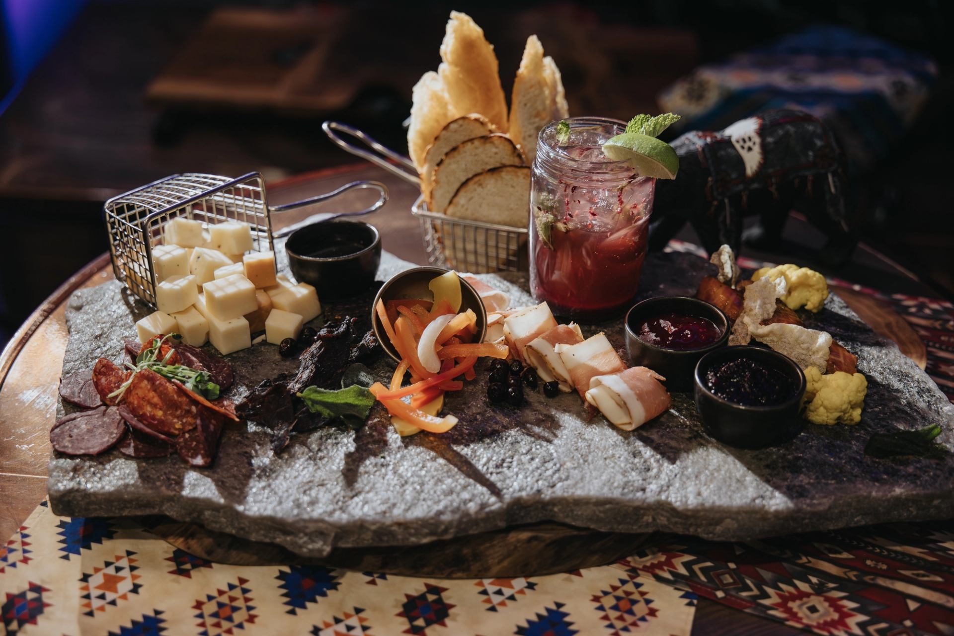 Charcuterie board with sliced meats, cheeses, pickled vegetables and a cocktail in a jar.