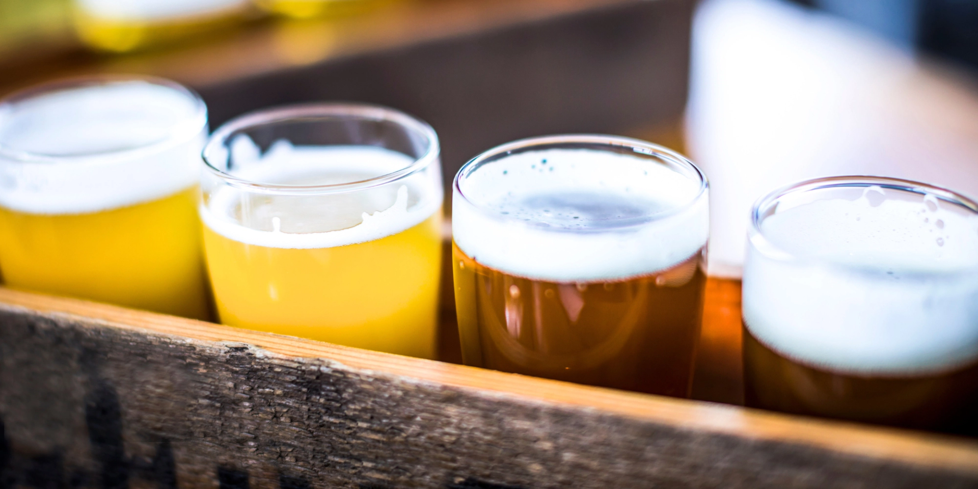 Flight of craft beer glasses resting on a wooden tray in soft light.