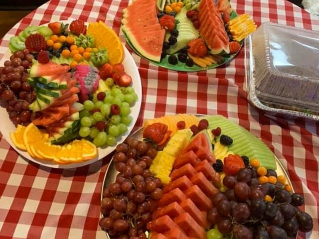 Three colorful fruit platters with watermelon, grapes, oranges, and berries on a red checkered tablecloth.