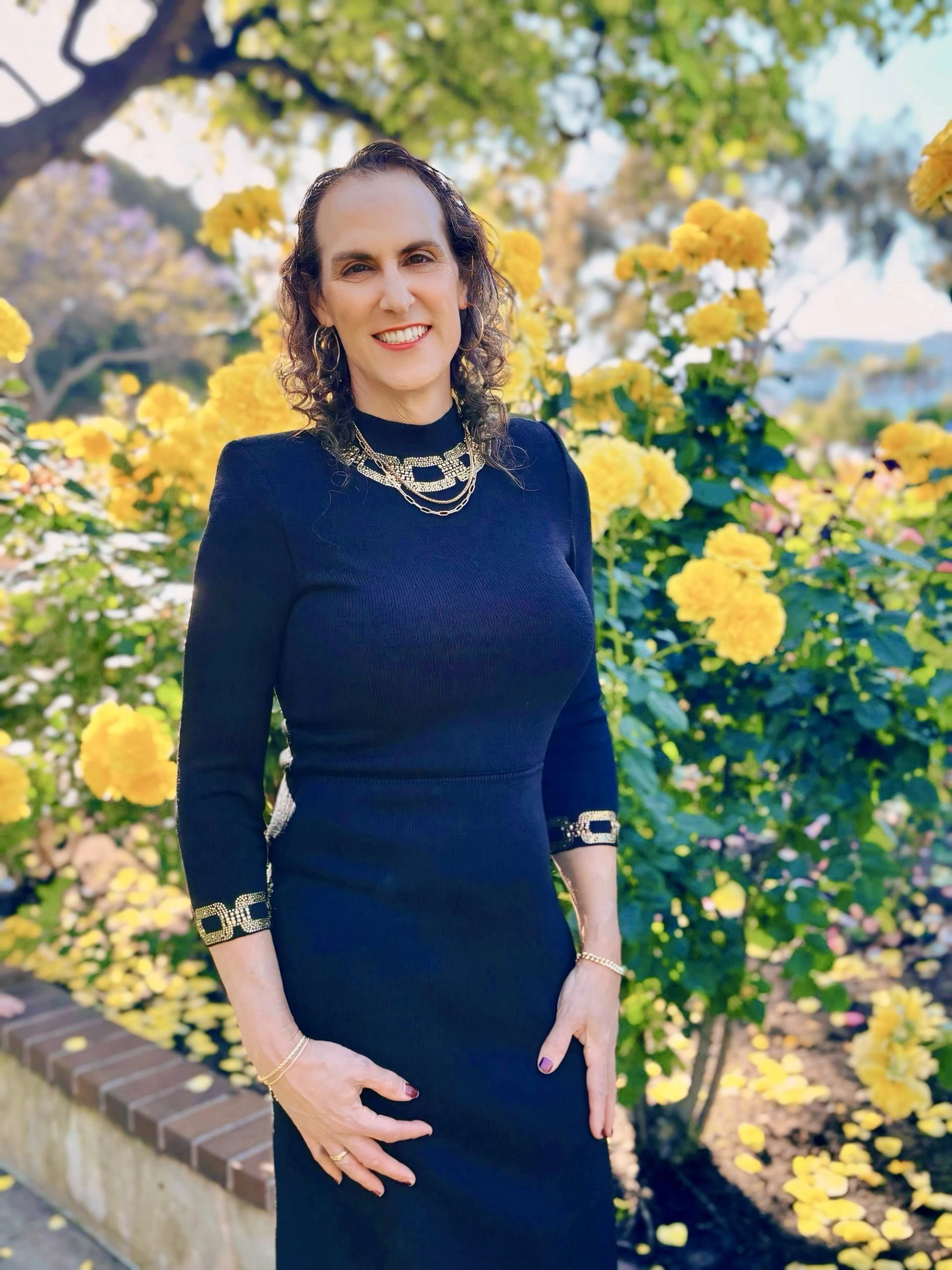 Person in dark dress stands in garden with bright yellow flowers and green foliage.