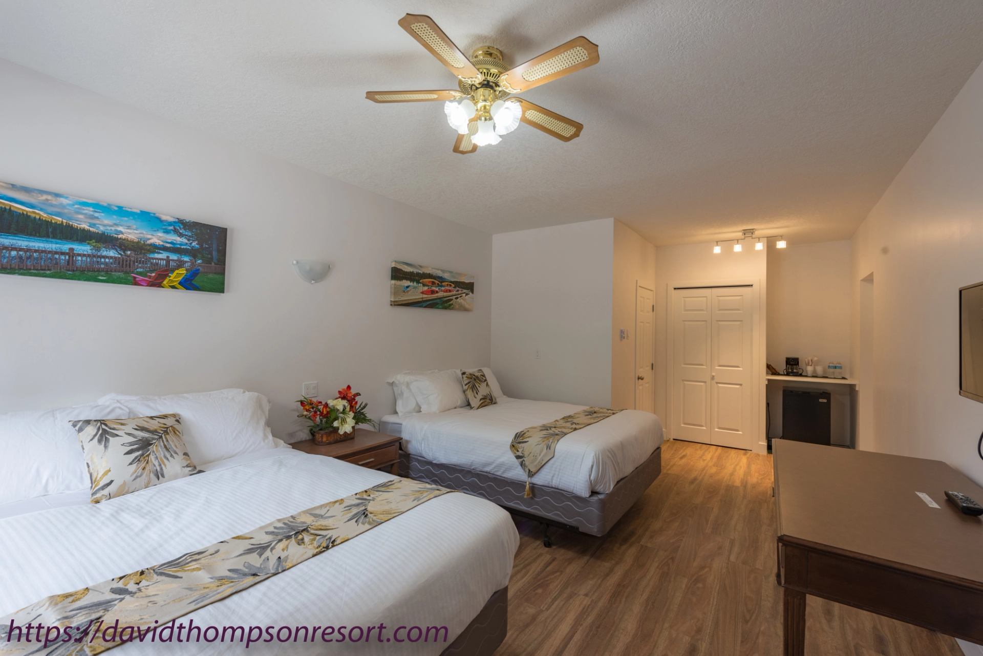 Guest room with two beds, floral accents, ceiling fan, mini-fridge and desk.