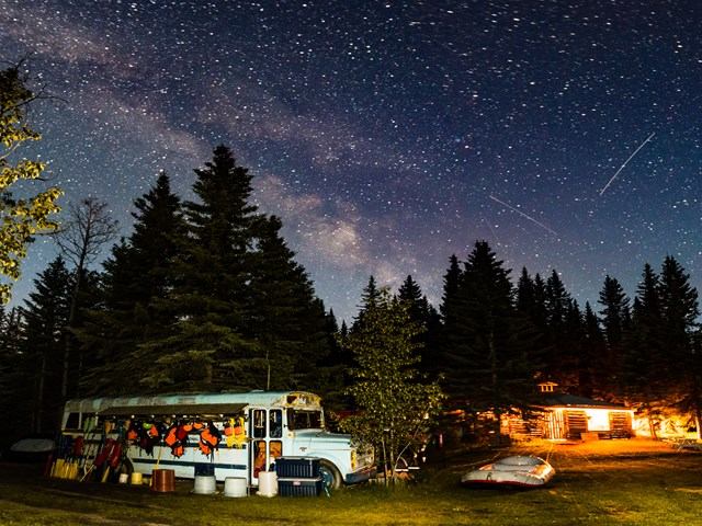 Night camping site with an RV and stars over a forest in the background.