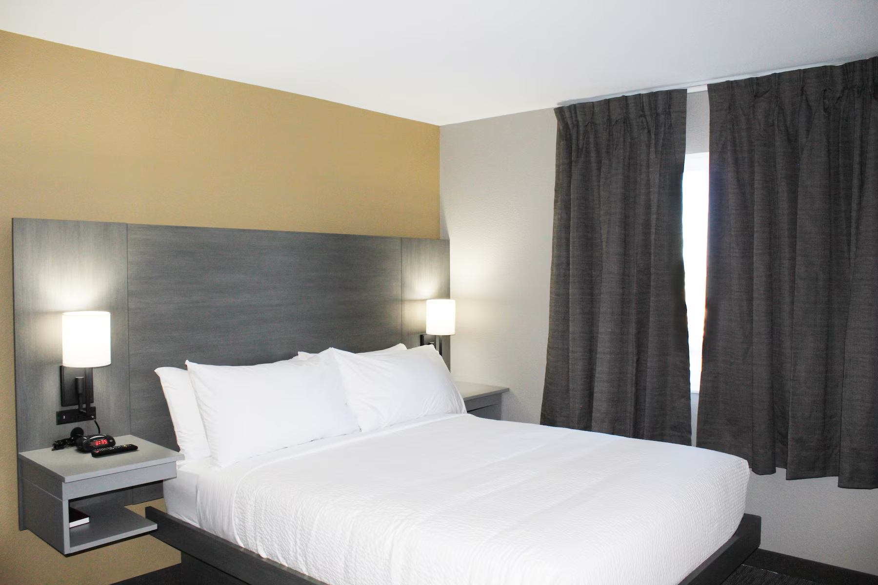 Guest room featuring a king bed, bedside lamps, nightstands, dark curtains, and modern furnishings.