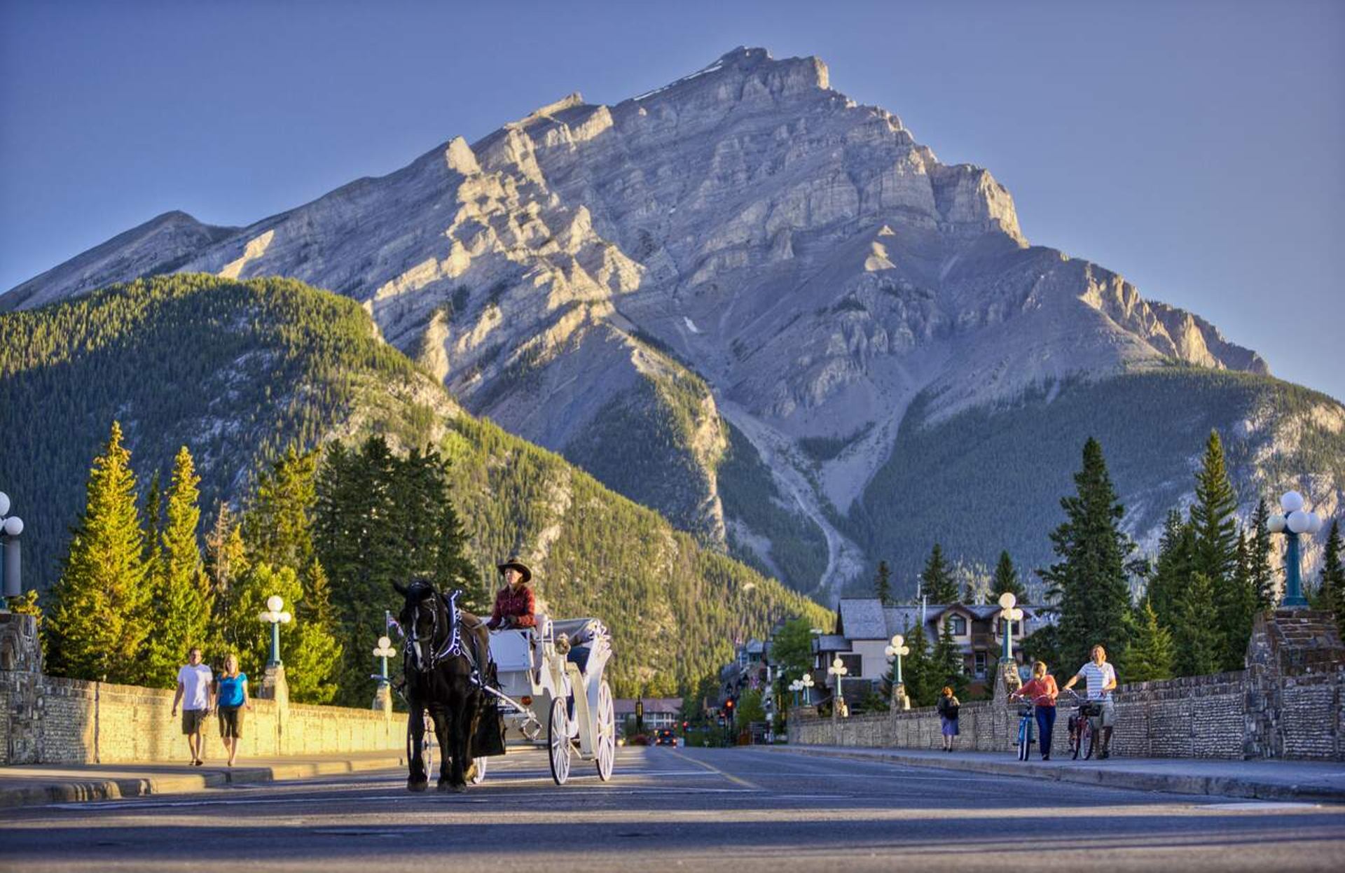 Horse-drawn carriage and pedestrians on mountain town street with towering rocky peak.