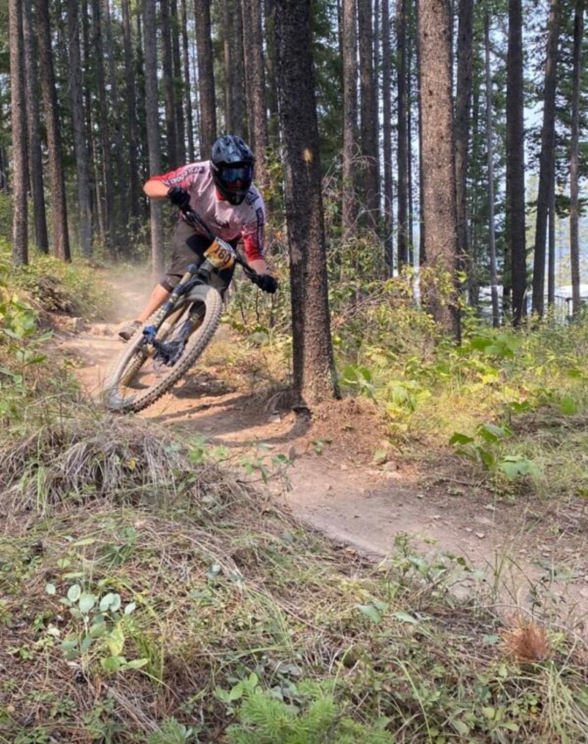 Mountain biker in helmet leans into a dirt trail corner through a forest.