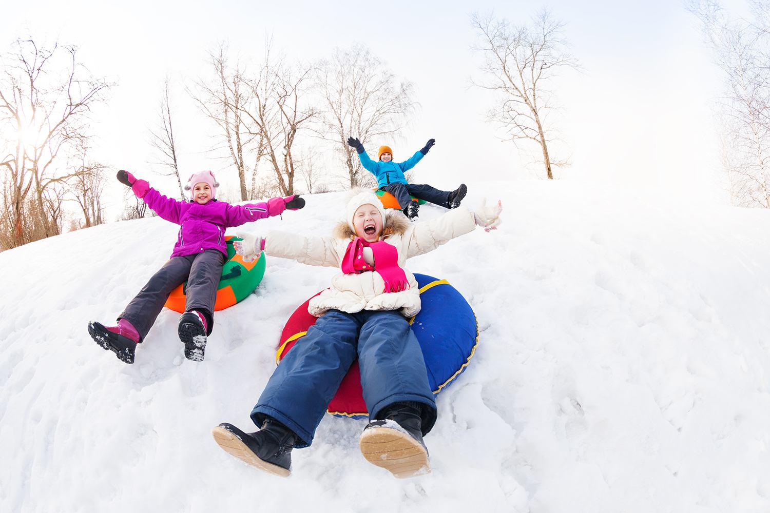 Children sledding on a snowy hill, wearing winter coats and snow boots outdoors.
