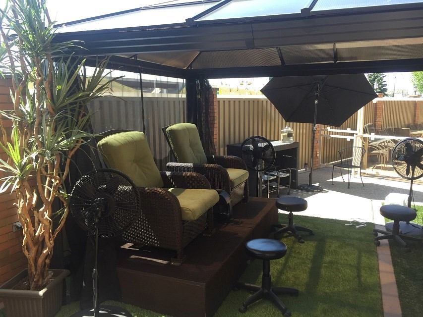 Covered patio with cushioned chairs, standing fans, stools and umbrella on green turf.