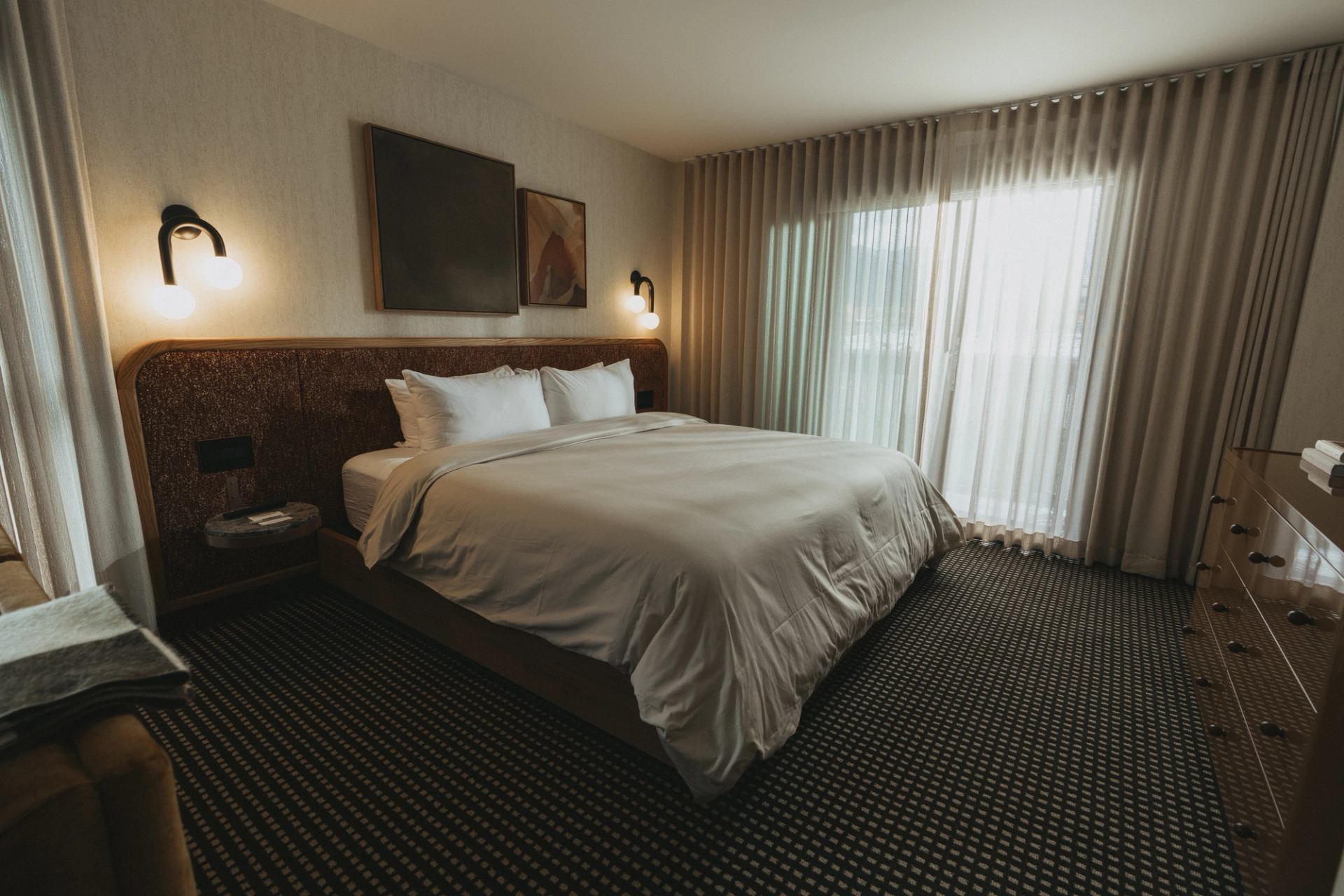Modern hotel bedroom with King bed, wood accents, white linens, and warm lighting.