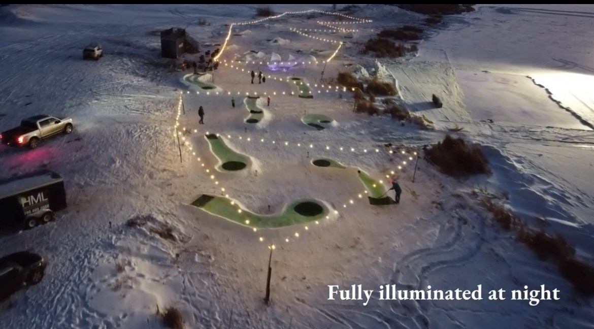 Minigolf course with illuminated paths and green holes on snowy ground at night.