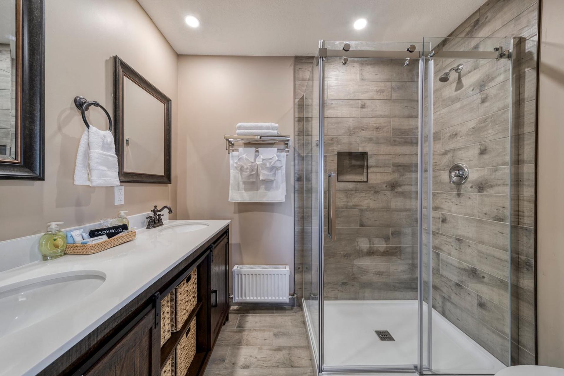 Modern bathroom with double-sink vanity, wicker baskets, towel rack and glass shower enclosure.