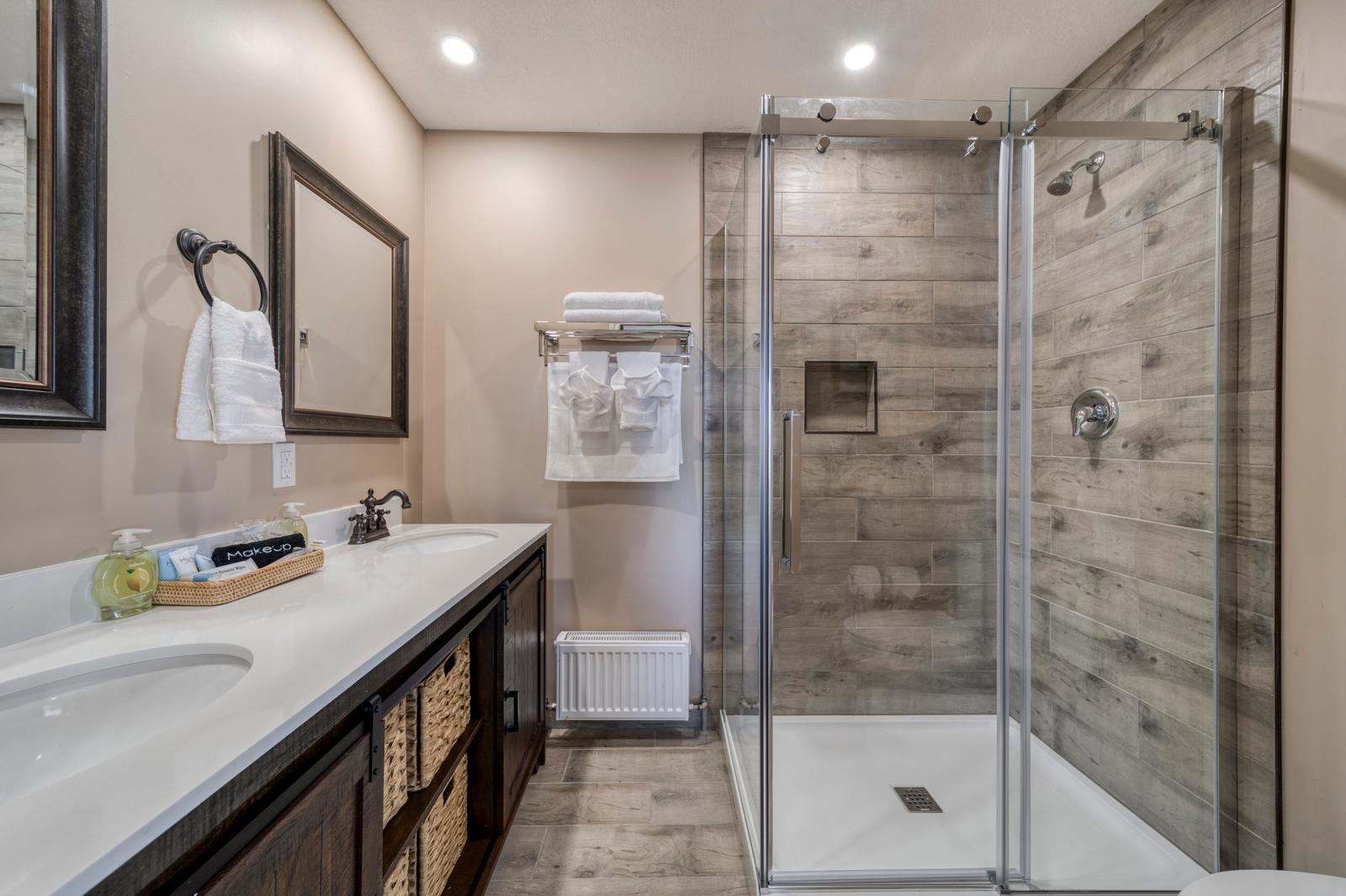 Modern bathroom with double-sink vanity, wicker baskets, towel rack and glass shower enclosure.