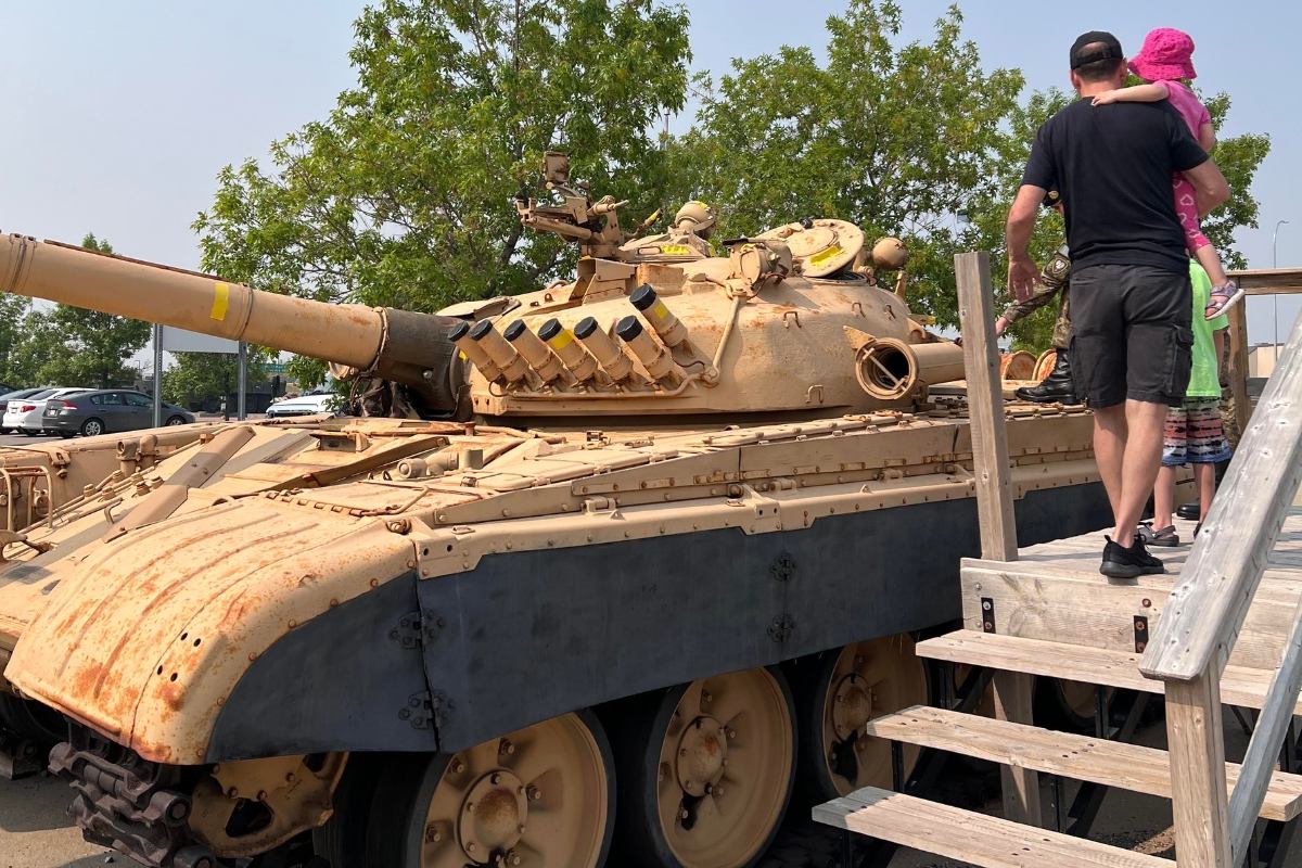 Armoured tank on display as visitors climb steps at an outdoor public exhibit in Calgary.