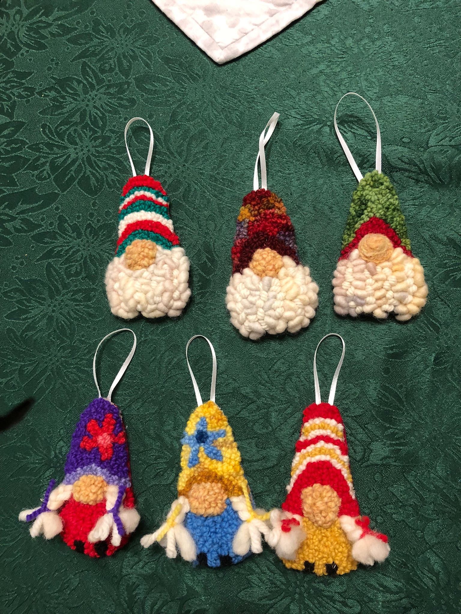 Embroidered Santa ornaments with hanging loops on textured green fabric background.