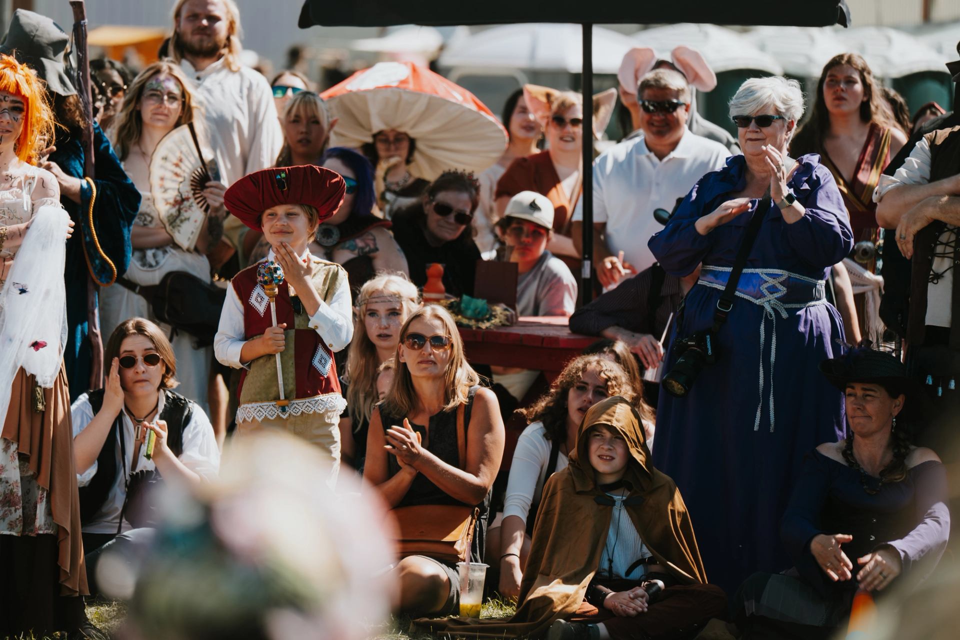 Audience members in medieval and fantasy attire watching a live performance at an outdoor festival setting.