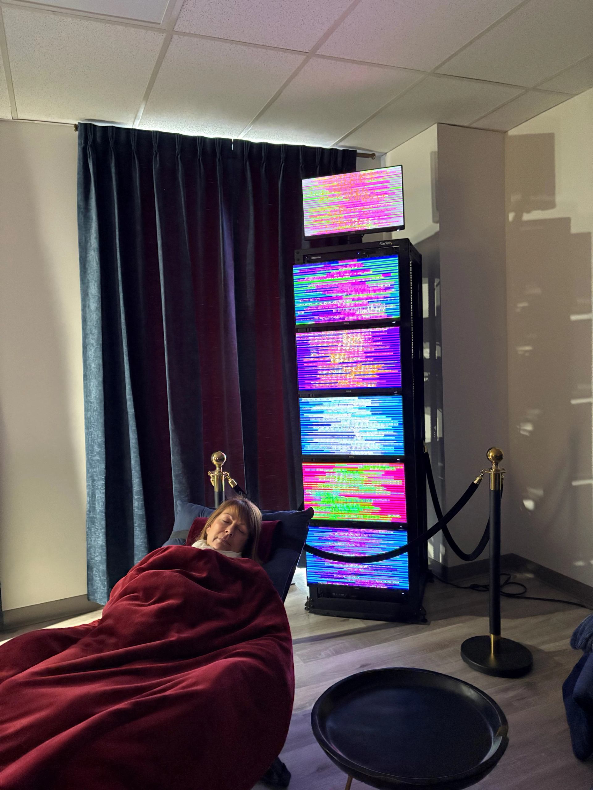 Person resting on recliner under red blanket beside tall colourful LED light panels