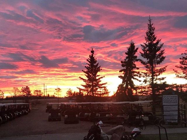 Golf carts lined up under vibrant red and orange sunset with silhouetted trees.