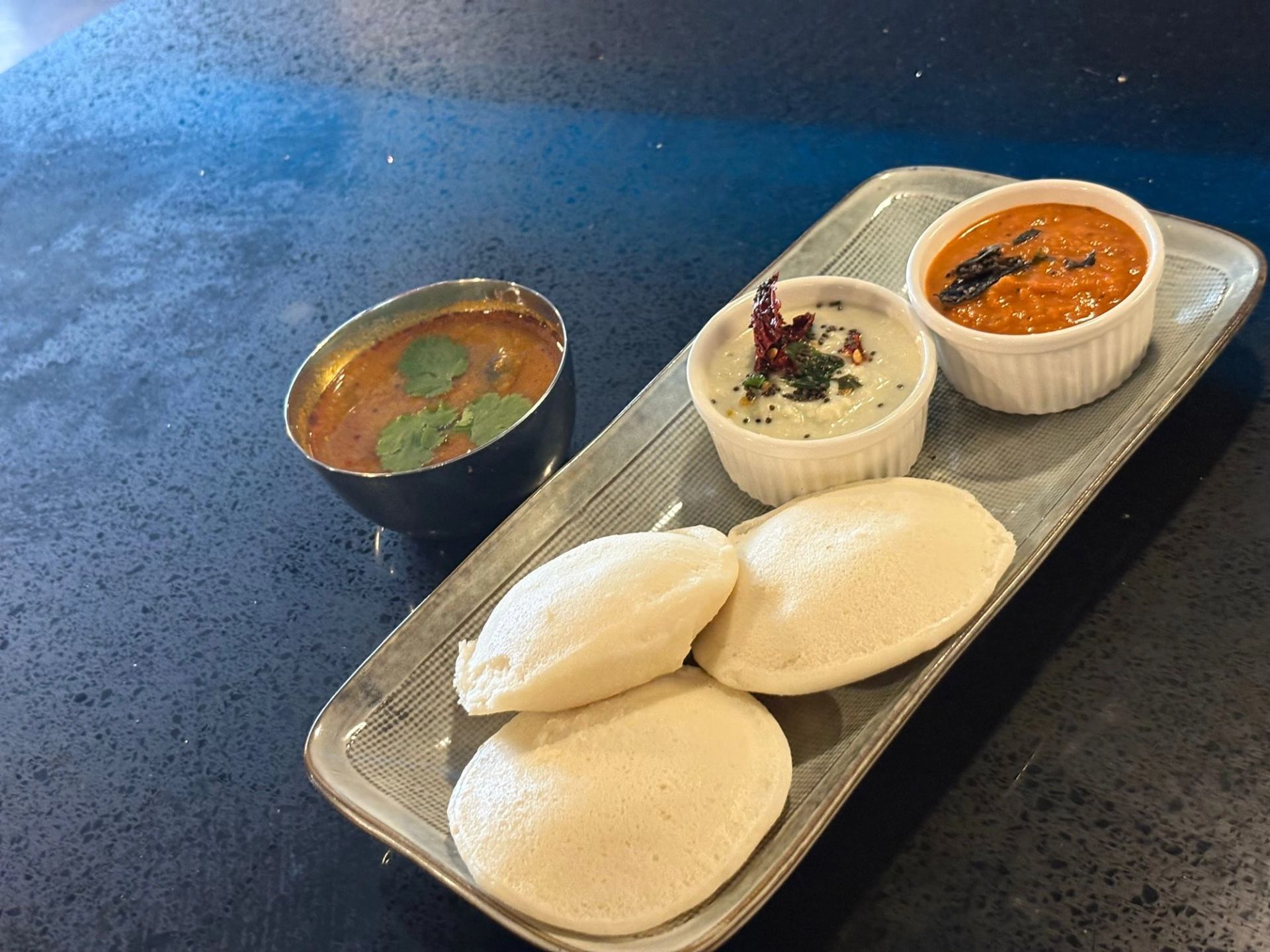 Plate of idlis with sambar, coconut chutney, and tomato chutney.