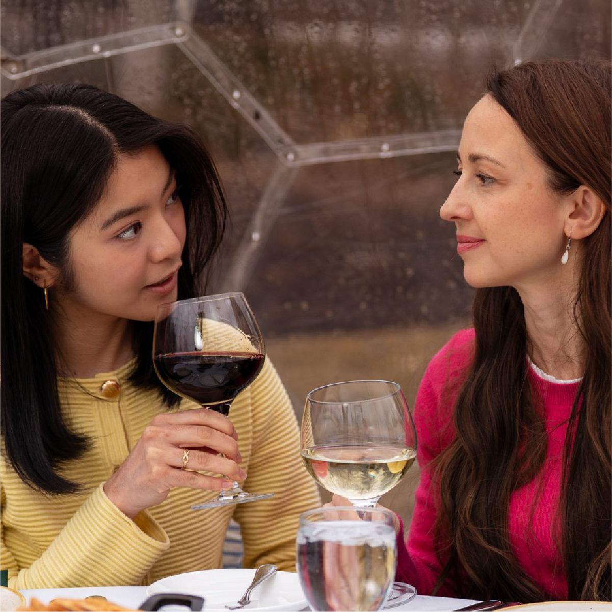 Two people converse at a table while holding glasses of red and white wine.