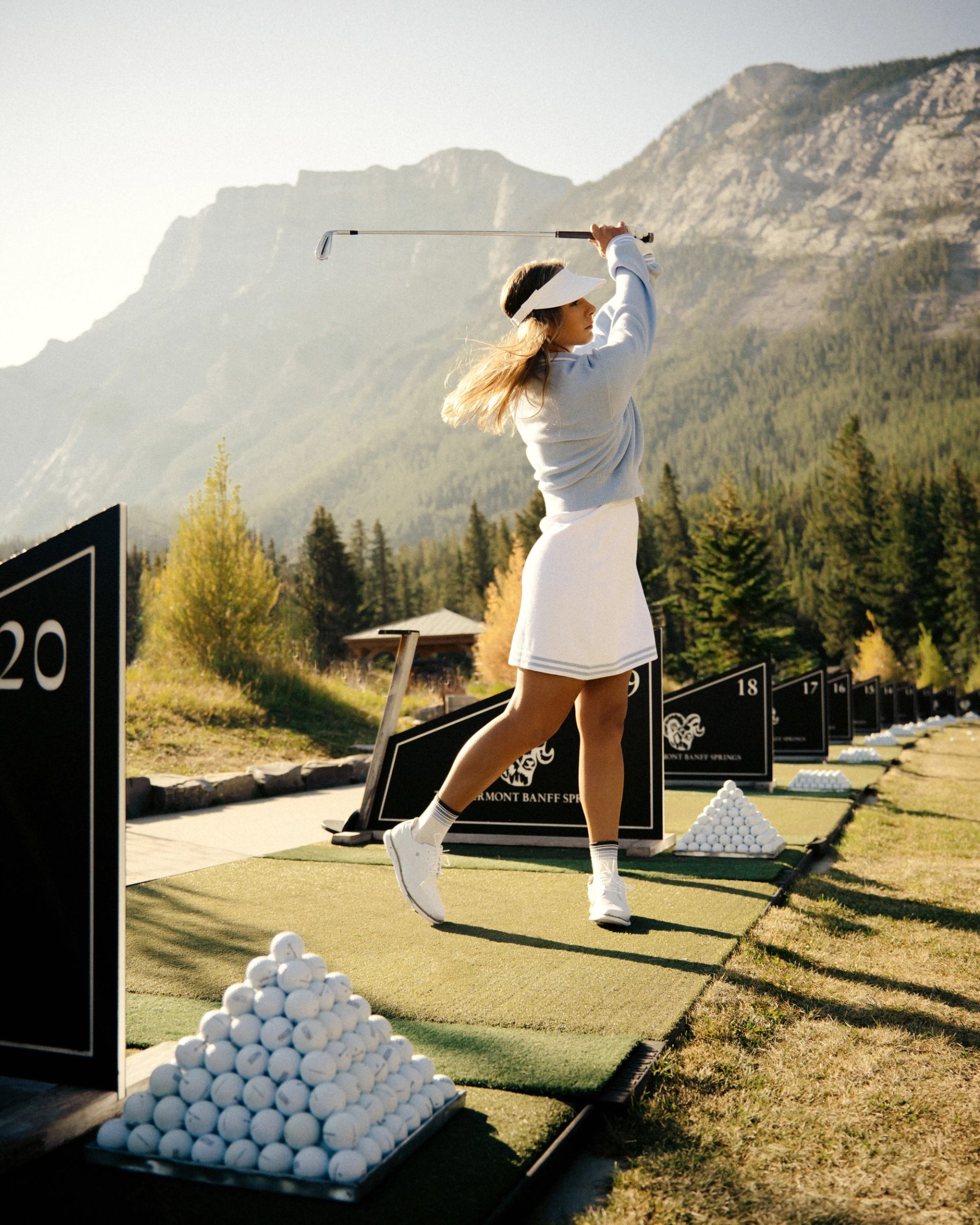 Golfer practicing a swing at Fairmont Banff Springs driving range with mountain backdrop.