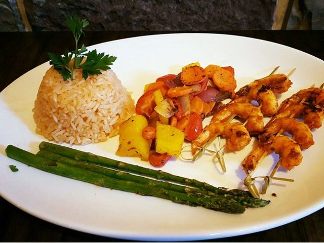 Plate with rice, grilled shrimp skewers, asparagus, and sautéed vegetables.