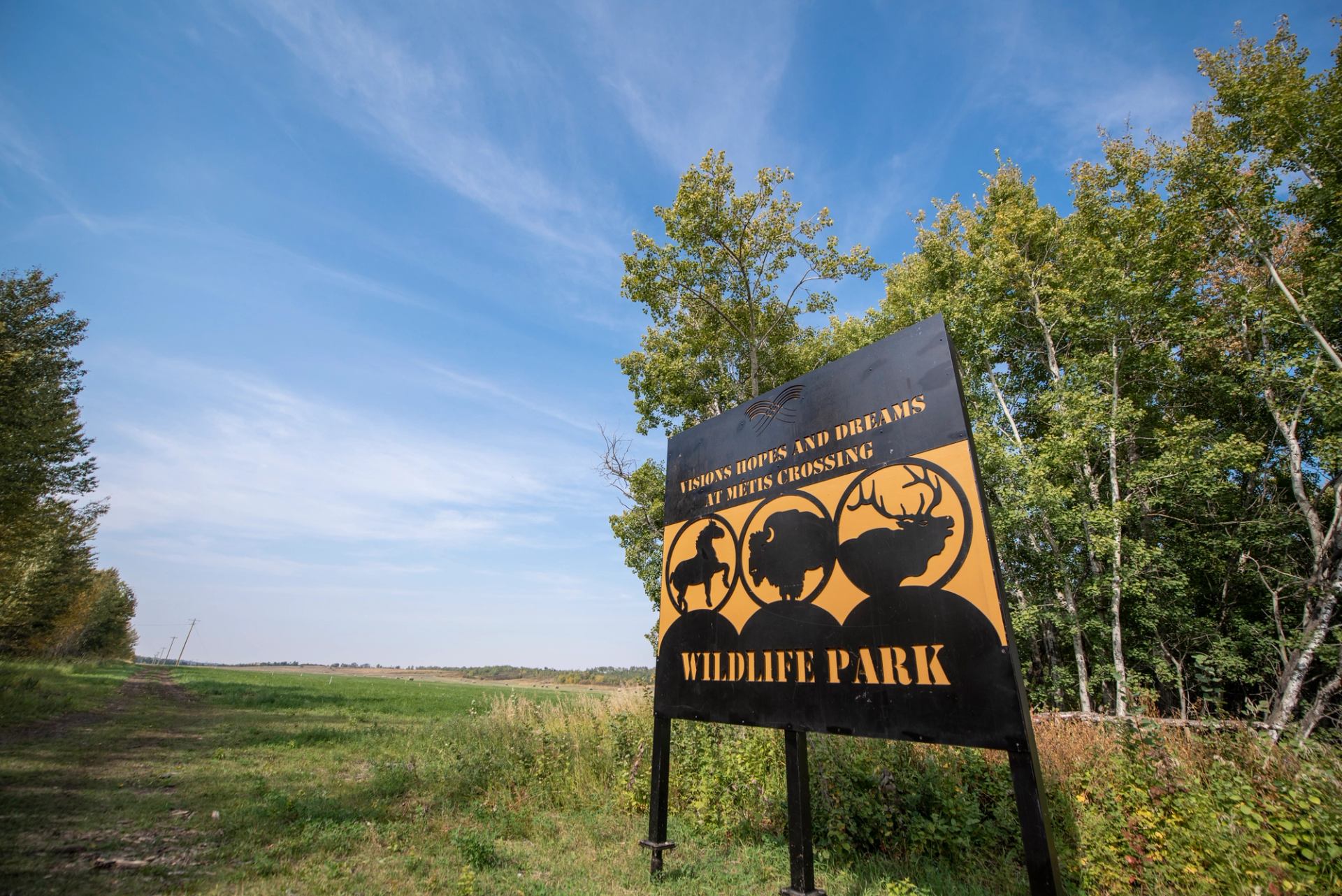 Wildlife Park entrance sign beside open grassy field and trees under blue sky.