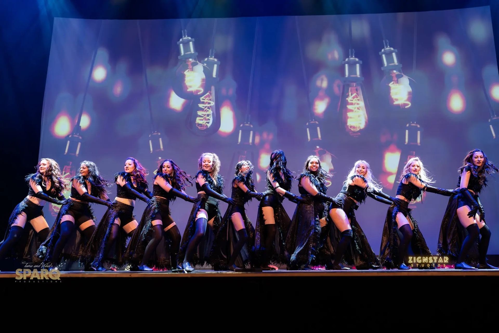 Performers pose in sync on stage with lanterns glowing in the backdrop.