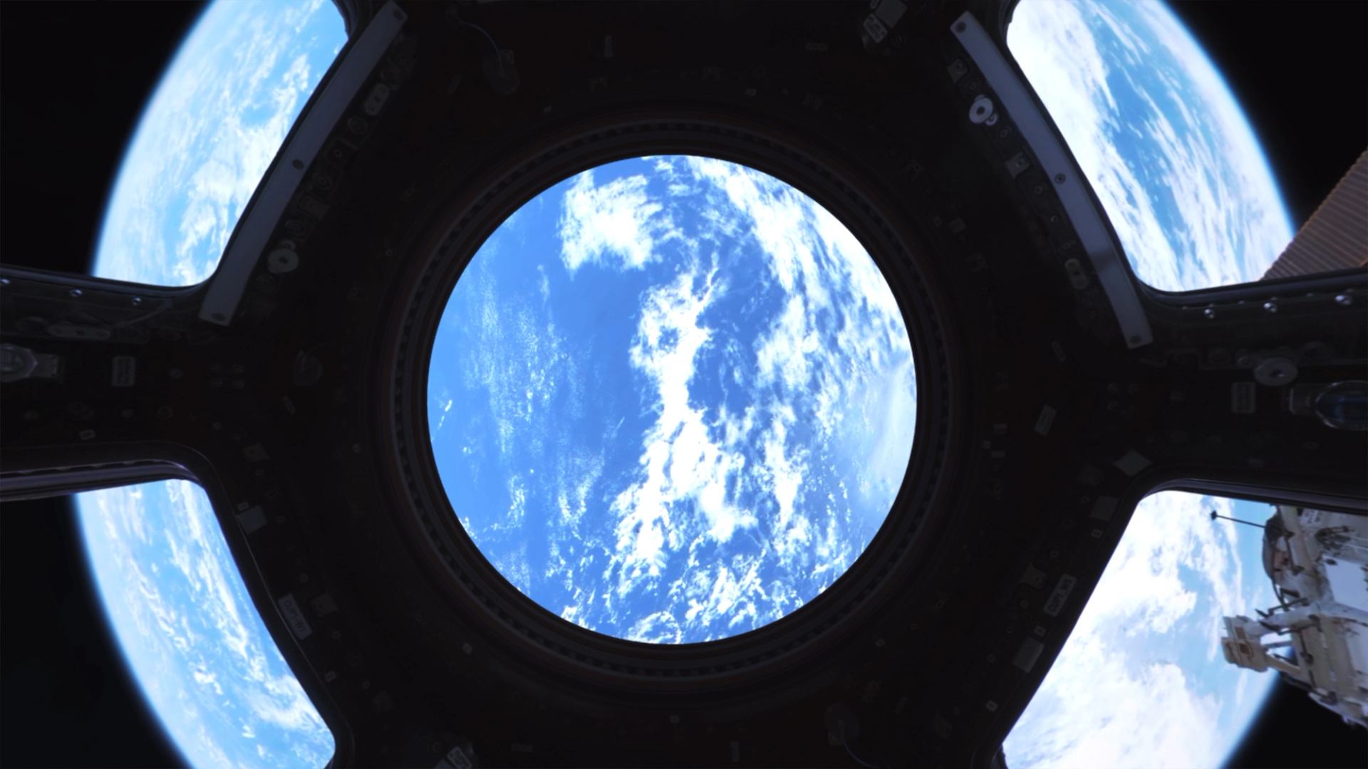 Spaceship window framing Earth clouds and sky, with astronaut equipment visible on right.