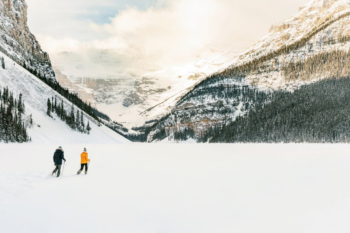 Two people walk across snowy mountain terrain near Lake Louise.