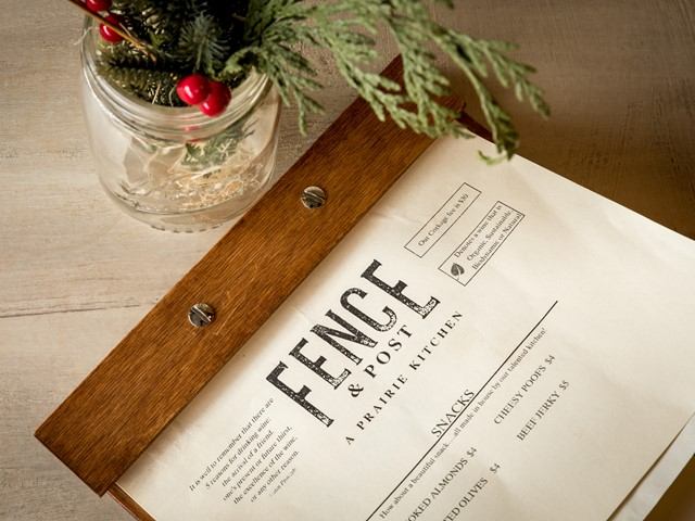 Fence & Post restaurant menu on wooden clipboard beside jar with evergreen branches and berries.